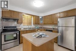 Kitchen featuring wood-finish cabinetry, stainless steel appliances, a center island with a light-toned countertop, a double basin sink, and a tiled backsplash - 