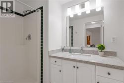 Bathroom featuring a white shower with dark accent tiles, a vanity with a light-colored speckled countertop, an undermount sink, and white cabinetry with dark hardware - 