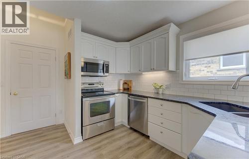 Kitchen featuring white shaker-style cabinetry, dark countertops, a stainless steel appliance suite, white subway tile backsplash, and light wood-finish flooring - 249 Dearborn Boulevard, Waterloo, ON - Indoor Photo Showing Kitchen