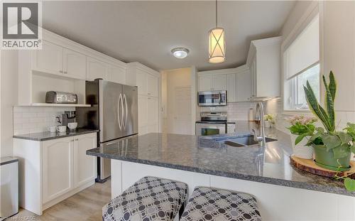 Kitchen featuring a large island with a sink, white cabinetry, stainless steel appliances, dark countertops, and light wood-finish flooring - 249 Dearborn Boulevard, Waterloo, ON - Indoor Photo Showing Kitchen With Upgraded Kitchen