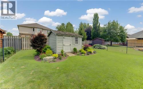 Expansive green lawn featuring a pale green storage shed with a shingled roof, a decorative garden bed with various plants and a large rock, and a wooden privacy fence - 249 Dearborn Boulevard, Waterloo, ON - Outdoor