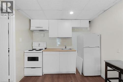 Compact kitchen featuring white cabinetry, a single basin stainless steel sink, wood-finish flooring, a white electric range, and a white refrigerator - 421 Bairstow Crescent, Waterloo, ON - Indoor Photo Showing Kitchen