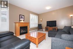 Carpeted living area featuring a central fireplace with a light wood mantel, light tan walls, and two windows with louvered shutters - 