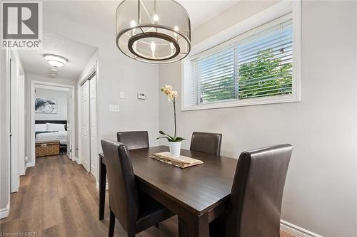 Dining area featuring a contemporary drum pendant light fixture, a large window with blinds, and wood-finish flooring - 50 Howe Drive Unit# 9D, Kitchener, ON - Indoor Photo Showing Dining Room