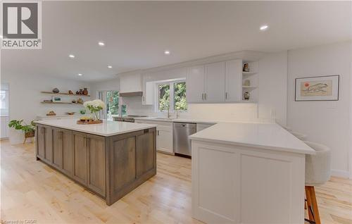 Spacious kitchen featuring a large wood-finish island with a light-toned countertop, white cabinetry with integrated lighting, a stainless steel dishwasher, and light wood-finish flooring - 307 Grand River Boulevard, Kitchener, ON - Indoor Photo Showing Kitchen