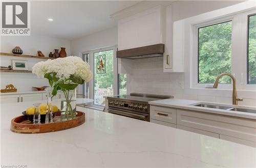Well-appointed kitchen featuring a substantial island with a light-toned countertop, white cabinetry with gold-toned hardware, a stainless steel range, and a white subway tile backsplash - 307 Grand River Boulevard, Kitchener, ON - Indoor Photo Showing Kitchen With Double Sink