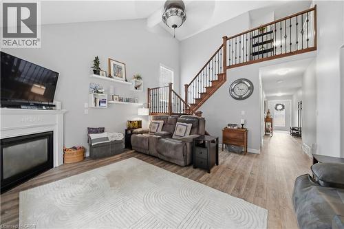 Living area with high ceilings, featuring a fireplace with a decorative mantel, wood-finish flooring, and a staircase with dark wood handrails and black metal spindles - 79 Beaverbrook Crescent, Cambridge, ON - Indoor With Fireplace