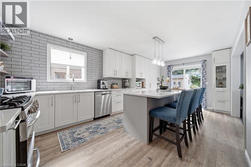 Modern kitchen featuring a central island with seating, extensive white cabinetry, stainless steel appliances, light wood-finish flooring, and a gray subway tile backsplash - 79 Beaverbrook Crescent, Cambridge, ON - Indoor
