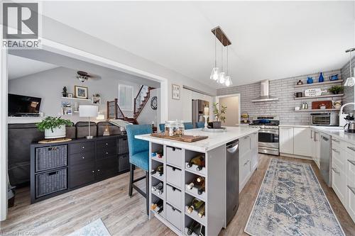 Kitchen featuring a large central island with integrated wine storage, white cabinetry, stainless steel appliances, a gray brick-patterned backsplash, and wood-finish flooring - 79 Beaverbrook Crescent, Cambridge, ON - Indoor Photo Showing Kitchen With Upgraded Kitchen