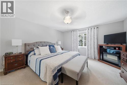 Carpeted bedroom featuring light gray walls, a ceiling fan with integrated lighting, a window with curtains, and a built-in media console with an electric fireplace - 79 Beaverbrook Crescent, Cambridge, ON - Indoor Photo Showing Bedroom