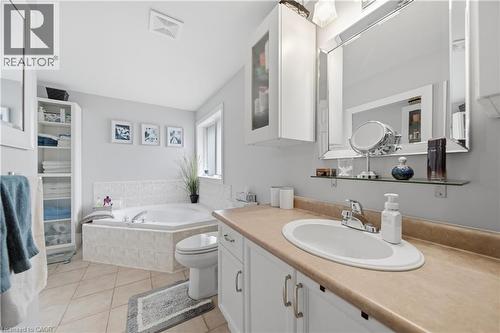 Bathroom featuring a built-in corner soaking tub with tile surround, a single vanity with an integrated sink and light-toned countertop, a mirrored vanity cabinet, and tiled flooring - 79 Beaverbrook Crescent, Cambridge, ON - Indoor Photo Showing Bathroom