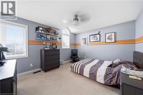 Carpeted room featuring dual windows, including an arched transom window, a ceiling fan with integrated lighting, and multiple wall-mounted shelves for display - 79 Beaverbrook Crescent, Cambridge, ON - Indoor Photo Showing Bedroom