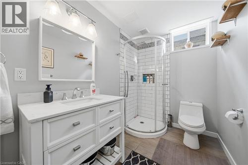 Bathroom featuring a white vanity with an integrated sink, a rounded glass-enclosed shower, subway tile surround, a low-profile toilet, and wood-finish flooring - 79 Beaverbrook Crescent, Cambridge, ON - Indoor Photo Showing Bathroom