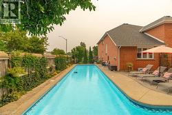 In-ground swimming pool with a concrete surround, bordered by a brick residence and a wooden fence with mature greenery - 