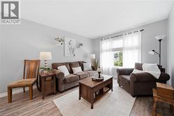 Spacious living area featuring wood-finish flooring, light gray walls, a large window with sheer white curtains, and recessed ceiling lighting - 