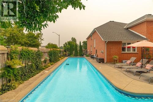 In-ground swimming pool with a concrete surround, bordered by a brick residence and a wooden fence with mature greenery - 79 Beaverbrook Crescent, Cambridge, ON - Outdoor With In Ground Pool