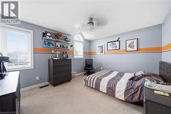 Carpeted room featuring dual windows, including an arched transom window, a ceiling fan with integrated lighting, and multiple wall-mounted shelves for display - 
