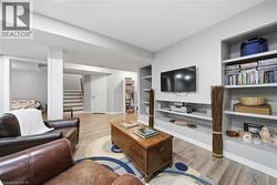 Spacious living area featuring light wood-finish flooring, built-in shelving, a dedicated media wall, and a separate stairway access - 