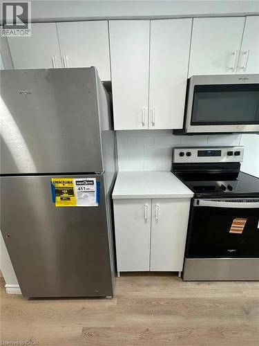Kitchen featuring stainless steel appliances, white cabinetry, a built-in microwave, white subway tile backsplash, and wood-finish flooring - 145 Macgregor Crescent Unit# 2 (R1), Waterloo, ON - Indoor Photo Showing Basement