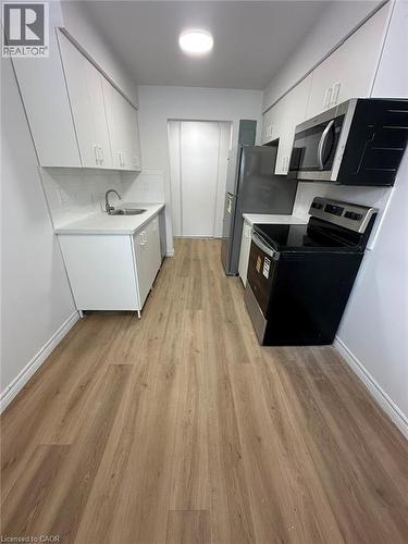 Galley kitchen featuring wood-finish flooring, white cabinetry, integrated stainless-steel appliances, white countertops, and a subway tile backsplash - 145 Macgregor Crescent Unit# 2 (R1), Waterloo, ON - Indoor Photo Showing Kitchen