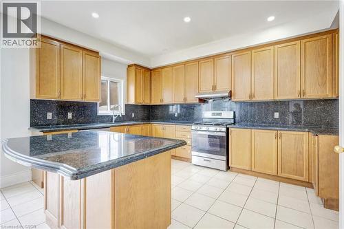 Kitchen featuring a central island with a dark stone countertop, extensive light wood cabinetry, a stainless steel range with overhead ventilation, and tiled flooring - 5 Freshspring Drive, Brampton, ON - Indoor Photo Showing Kitchen