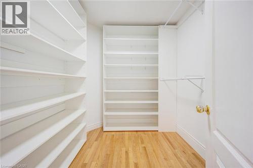 Walk-in closet featuring light wood-finish flooring, white built-in shelving, white walls, and a white interior door with a brass-finish doorknob - 5 Freshspring Drive, Brampton, ON - Indoor