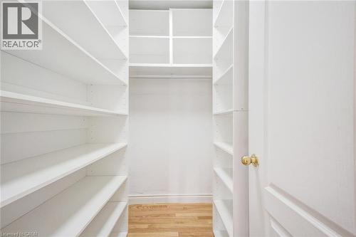 Walk-in closet featuring extensive built-in white shelving, upper storage compartments, and wood-finish flooring - 5 Freshspring Drive, Brampton, ON - Indoor With Storage
