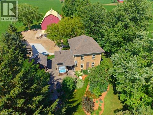 Expansive property featuring a multi-story brick residence, a red barn with a yellow roof, a covered outdoor spa, and a stone patio - 8430 Road 146, Listowel, ON - Outdoor