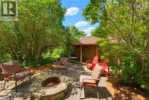 Stone-paver patio featuring a built-in stone fire pit, surrounded by lush mature trees and plantings - 8430 Road 146, Listowel, ON - Outdoor