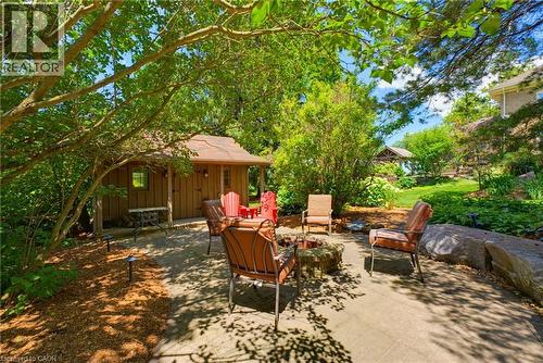 Stone patio featuring a built-in fire pit, surrounded by lush landscaping and mature trees - 8430 Road 146, Listowel, ON - Outdoor