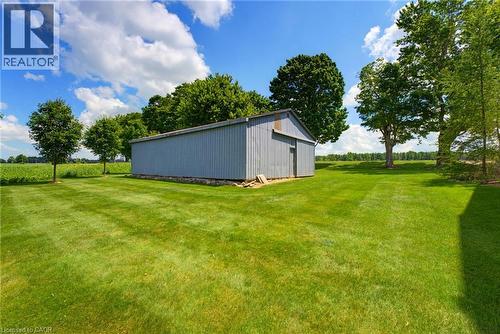 Expansive green lawn featuring a corrugated metal outbuilding with a sliding door, established shade trees, and clear sky overhead - 8430 Road 146, Listowel, ON - Outdoor