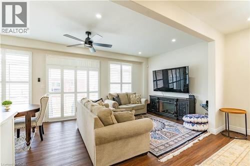 Open-concept living area featuring wood-finish flooring, white plantation shutters, recessed lighting, a ceiling fan, and a built-in electric fireplace with an ornate dark wood console - 122 Iron Gate Street, Kitchener, ON - Indoor Photo Showing Living Room With Fireplace