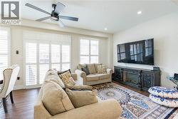 Spacious living area featuring wood-finish flooring, white plantation shutters, an integrated fireplace unit, recessed lighting, and a ceiling fan - 