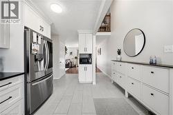 Contemporary tile flooring leading to a full kitchen featuring a stainless steel refrigerator, white cabinetry with dark hardware, and dark countertops - 