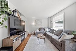 Bright interior featuring wood-finish flooring, a contemporary media console with built-in storage, and a large window with horizontal blinds - 