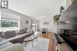 Open-concept living space featuring wood-finish flooring, a large window with white blinds, and a sliding glass door leading outdoors - 