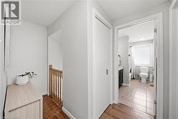Hallway with wood-finish flooring and light gray walls, leading to a bathroom with tile flooring, a white vanity with a dark base, and a window - 