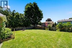 Expansive backyard featuring a lush lawn, established perimeter fencing, mature trees, a built-in fire pit, and a raised garden bed - 