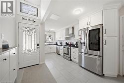 Contemporary kitchen and entryway featuring white cabinetry, stainless steel appliances, light tile flooring, a decorative front door with ironwork, and a transom window with stained glass - 