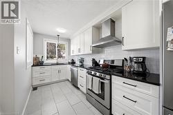 Kitchen featuring white cabinetry, black countertops, stainless steel appliances, white subway tile backsplash, and light-toned tile flooring - 