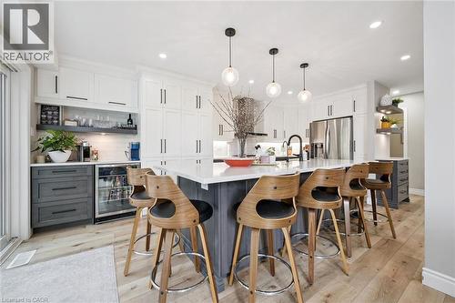 Spacious kitchen featuring a large island with seating, white shaker-style cabinetry, wood-finish flooring, a built-in beverage refrigerator, and pendant lighting - 916 Rush Meadow Court, Kitchener, ON - Indoor