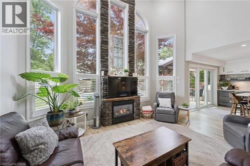 Vaulted ceiling living area featuring a stacked stone fireplace with a wood-finish mantle, large arched and rectangular windows, wood-finish flooring, and a kitchen with two-tone cabinetry - 916 Rush Meadow Court, Kitchener, ON - Indoor Photo Showing Living Room With Fireplace