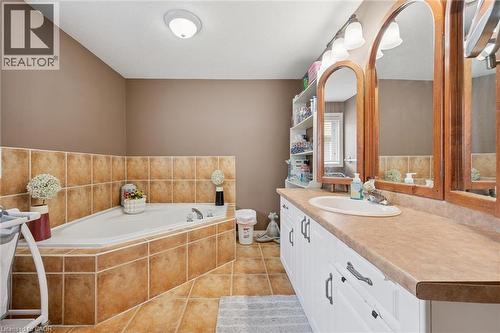 Bathroom featuring an angled soaking tub with tile surround, a double vanity with white cabinetry, a light-colored countertop, and individual wood-framed mirrors - 916 Rush Meadow Court, Kitchener, ON - Indoor Photo Showing Bathroom