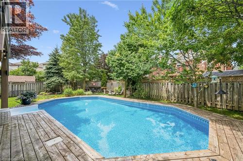 Fenced backyard featuring an in-ground swimming pool, surrounding wood decking, mature trees, and established landscaping - 916 Rush Meadow Court, Kitchener, ON - Outdoor With Backyard