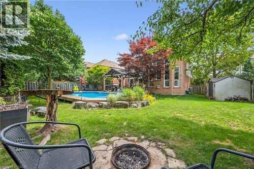 Expansive backyard featuring a central lawn, a built-in fire pit with stone surround, and an inground pool with a surrounding wood deck - 916 Rush Meadow Court, Kitchener, ON - Outdoor With Backyard