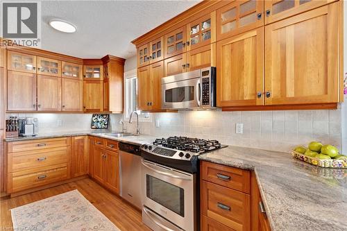 Kitchen featuring rich wood cabinetry with some upper glass-front doors, stone countertops, stainless steel appliances, and a tiled backsplash - 350 Doon Valley Drive Unit# 6D, Kitchener, ON - Indoor Photo Showing Kitchen