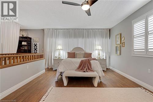 Bedroom featuring wood-finish flooring, plantation shutters, full-height white drapery, a ceiling fan with integrated lighting, and a partial wood railing - 350 Doon Valley Drive Unit# 6D, Kitchener, ON - Indoor Photo Showing Bedroom