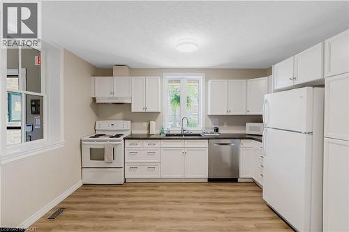 Kitchen featuring white cabinetry, dark countertops, a stainless steel dishwasher, and wood-finish flooring - 350 Doon Valley Drive Unit# 6D, Kitchener, ON - Indoor Photo Showing Kitchen