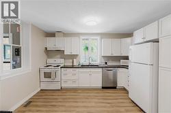 Kitchen featuring white cabinetry, dark countertops, a stainless steel dishwasher, and wood-finish flooring - 