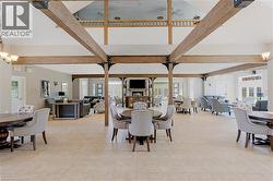 Spacious common area featuring vaulted ceilings with exposed wood beams, neutral tile flooring, a built-in fireplace, and large windows providing ample natural light - 